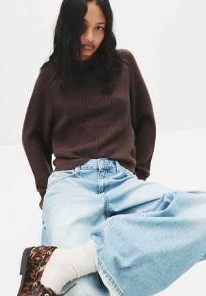 Ruskea ribattu neule, vaaleansiniset löysät farkut, kuviolliset nilkkurit. Neuleessa on korkea kaulus; farkuissa on rento istuvuus ja denim-kudos.