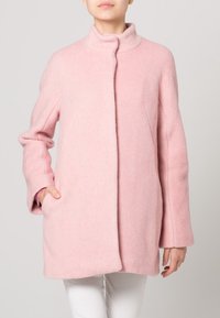 Abrigo de lana rosa con un cuello alto, corte recto, mangas largas y bolsillos laterales; textura suave y diseño minimalista.