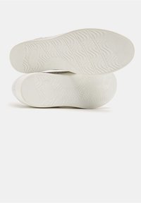 Fehér sneaker talpak texturált hullám mintával, kör alakú sarkakkal és kis márkajelzésekkel. Lapított és rugalmas kialakítás.