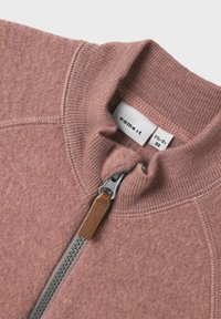 Fleece-Zip-Jacke in staubigem Rosé, mit hohem Kragen, metallic-farbenem Reißverschluss mit einem braunen Leder-Zugband und strukturiertem Stoff.