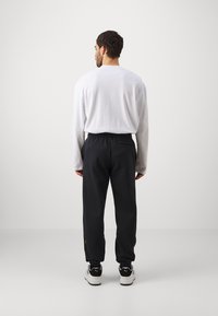 Pantalones jogger negros con cinturilla elástica, bolsillos laterales y un detalle de acento amarillo. Combinados con una camiseta larga blanca de corte suelto.