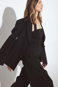 Czarna, oversize żakiet z wyraźnie zarysowanymi ramionami, połączony z dopasowanym czarnym topem i spodniami w szerokie nogawki, tworzy elegancką sylwetkę.