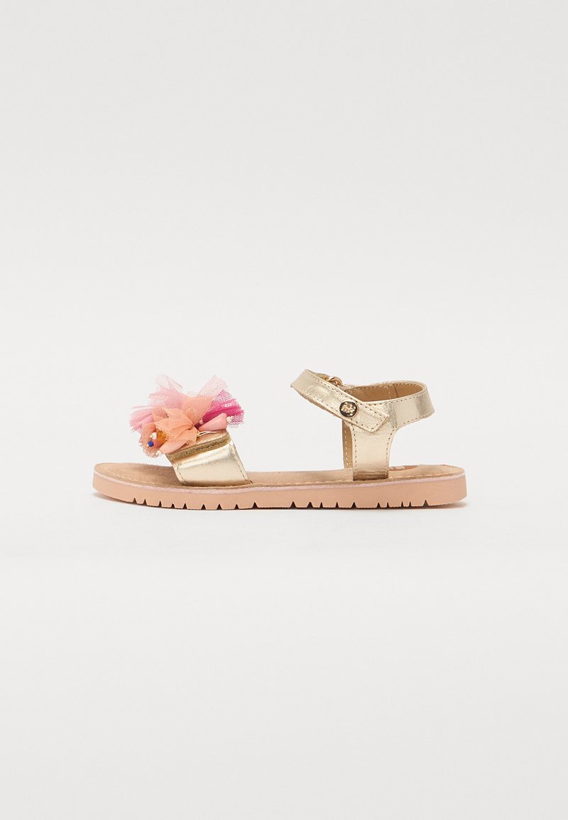 Sandale métallique dorée avec un accent de fleur en tulle rose et orange, sangle réglable et semelle texturée beige. Design plat pour un maximum de confort.