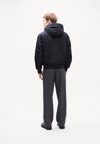 Veste à capuche noire au toucher lisse, assortie à un pantalon gris à motifs. L'ensemble présente une silhouette décontractée et un style casual.