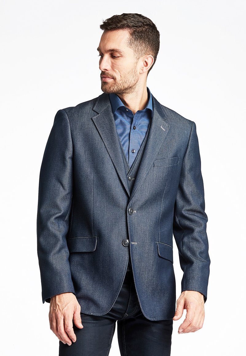 Dunkelblazer aus strukturiertem Stoff, mit zwei Knöpfen, Reverskragen und praktischen Fronttaschen. Trägt einen blauen Hemd.