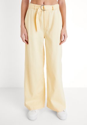 Pantalones de pierna ancha hechos de suave algodón en un amarillo pálido, con una cintura con cinturón y anillo D plateado, y un dobladillo a la altura del tobillo.