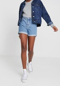 Jeansjacka, ljusblå shorts, grå t-shirt, vita sneakers. Shortsen har uppvikta fållar; jackan har knappar och fickor.