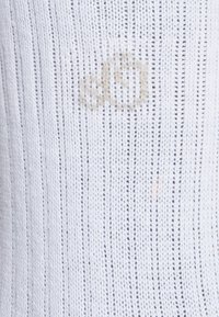 Tessuto lavorato a maglia bianco con strisce verticali. Macchia leggera e poco visibile al centro, di un colore leggermente avorio. Texture liscia, materiale leggero.