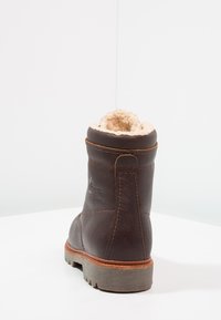 Bota de couro castanho com forro creme fofinho, bico redondo e sola bege. Apresenta detalhes de costura e uma marcação em relevo na lateral.