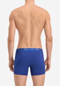 Blaue Boxershorts aus einem dehnbaren Material, mit einem elastischen, markierten Bündchen, auf dem "PUMA" in fetten, kontrastierenden Buchstaben steht.
