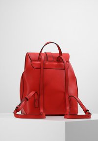 Zaino in pelle rossa con un design strutturato, dotato di chiusura a pattina, rifiniture nere a contrasto, spallacci regolabili e una finitura testurizzata.