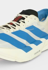 Λευκό και μπλε αθλητικό παπούτσι με σόλα Light Strike Pro, λευκά κορδόνια και μαύρη γλώσσα με κόκκινο κείμενο "ADIZERO".