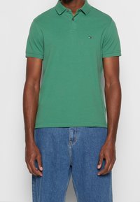 Green cotton polo shirt with a buttoned collar, short sleeves, and a small logo on the chest; paired with blue denim jeans.