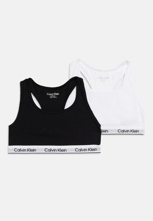 Δύο αθλητικά σουτιέν Calvin Klein, ένα μαύρο και ένα λευκό, με ελαστικές ταινίες με το λογότυπο στο κάτω μέρος, τοποθετημένα επίπεδα σε λευκό φόντο.