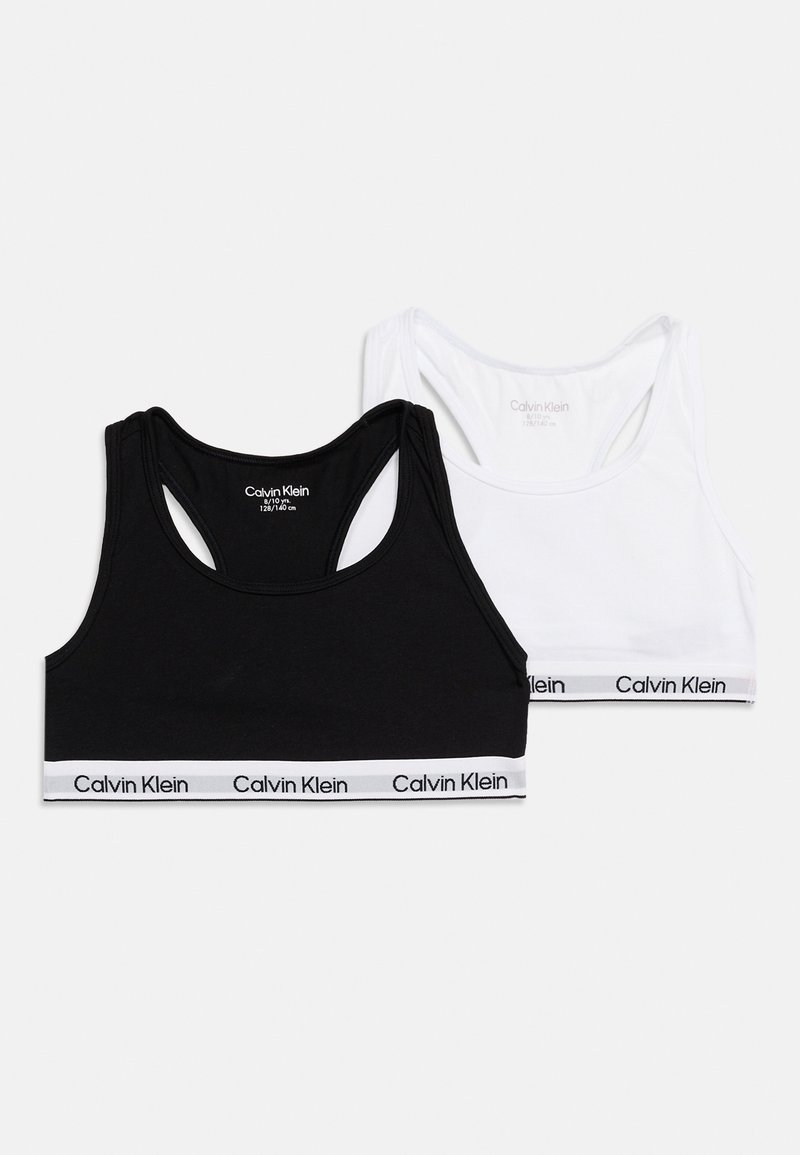 Δύο αθλητικά σουτιέν Calvin Klein, ένα μαύρο και ένα λευκό, με ελαστικές ταινίες με το λογότυπο στο κάτω μέρος, τοποθετημένα επίπεδα σε λευκό φόντο.