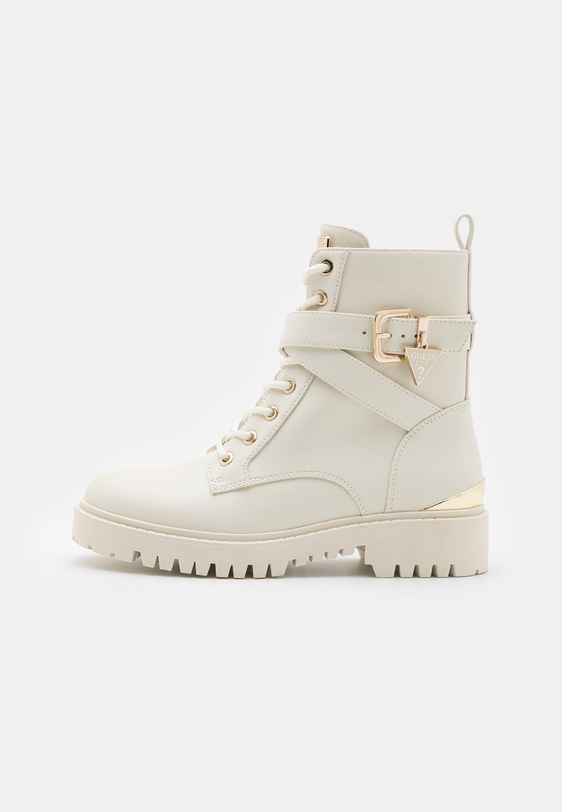 Botte en cuir crème montant jusqu'à la cheville avec lacets à l'avant, bride décorative avec boucle dorée, semelle crantée et accent doré sur le talon.