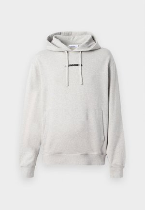 Sudadera gris claro hecha de tejido suave. Cuenta con un bolsillo frontal, capucha con cordón y un logotipo en texto negro en el pecho. Los puños son de canalé.