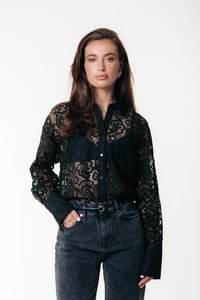 Camicia in pizzo nero con motivi floreali, chiusura frontale con bottoni e maniche lunghe, abbinata a jeans scuri a vita alta.