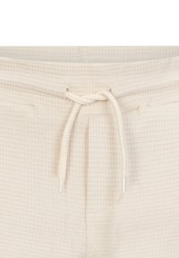 Helle beige Jogginghose mit strukturiertem Obermaterial und Rippmuster, Kordelzugbund und Metallspitzen. Weicher Stoff mit lässiger Passform.