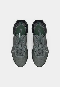 Scarpe sportive grigie con tomaia in rete testurizzata, dettagli verdi e particolari riflettenti. Presentano una suola nera resistente e un design con lacci.