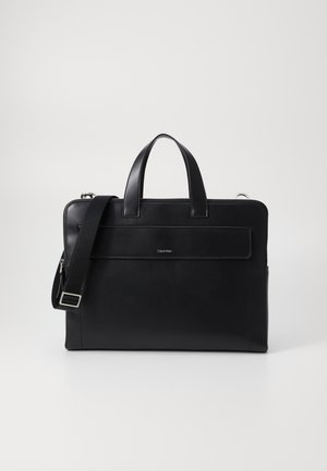 Valigetta nera in pelle con doppi manici, tracolla staccabile, tasca frontale con zip e dettagli logo discreti. Texture liscia e forma rettangolare.