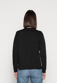 Musta svetari, jossa on pyöreä pääntie ja pitkät hihat, yksinkertainen ja koristelematon malli. Yhdistetty vaaleansinisiin farkkuihin.