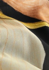 Țesătură țesută cu o textură de plasă, cu modele negre, galbene și piersici. Materialul este ușor și se așază moale.