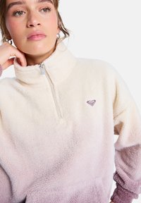 Fleece trui met een gradient van crème naar lichtroze. Heeft een halve rits, hoge kraag en een hartvormig logo op de borst.