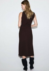 Vestido marrón sin mangas con una silueta fluida, que llega a la mitad de la pantorrilla, combinado con botas negras de tobillo holgadas. Diseño sencillo, textura suave.