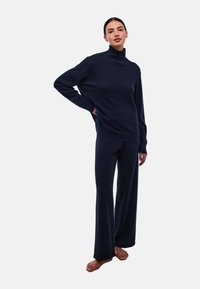 Pull en maille douce, bleu marine, avec col roulé et épaules tombantes, associé à un pantalon large assorti. Texture lisse, coupe décontractée.