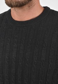 Suéter negro de punto con un diseño de trenzas texturizado y un cuello redondo de canalé, que resalta una apariencia suave y acogedora.