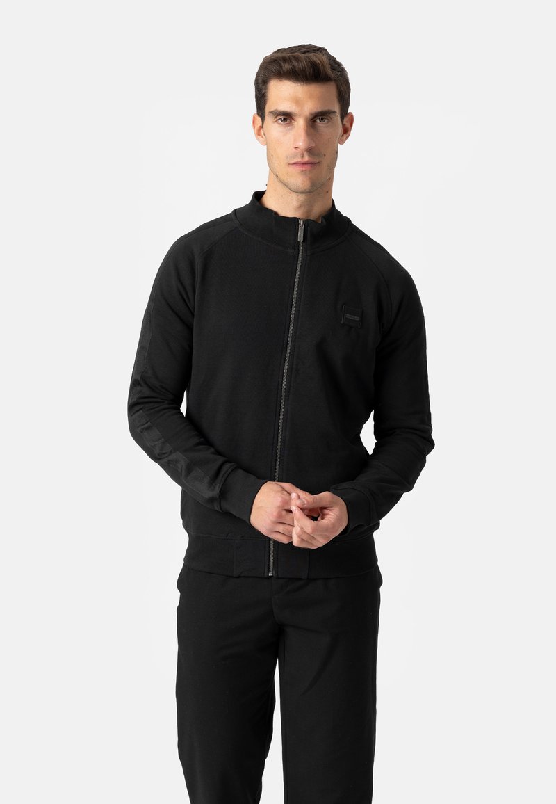 Zwarte sportjas met ritssluiting, hoge kraag, gestructureerde stof en zijzakken. Slim fit met contrasterende paneeldetails op de armen.