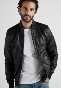 Schwarze Lederbomberjacke mit Reißverschluss vorne, gerippten Ärmelbündchen und seitlichen Taschen, die eine glatte Textur und minimalistisches Design aufweist.