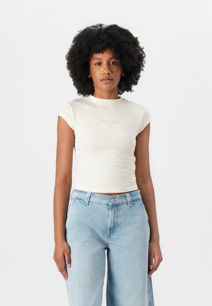 Light cream short-sleeve fitted t-shirt with a round neckline and graphic print on the chest, paired with light blue high-waisted jeans.