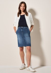 Jupe en denim près du corps avec poches avant, couleur bleu délavé et fermeture à bouton à la taille. Assortie avec un haut marine et des baskets blanches.