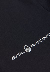 La tela azul marino presenta una superficie texturizada con un logo en blanco de "SAIL RACING" y un gráfico circular. El diseño es simple y moderno, con un enfoque en la funcionalidad.