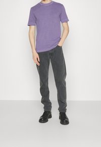 Fioletowa bawełniana koszulka z krótkim rękawem, uzupełniona ciemnoszarymi dżinsami. Czarne buty na sznurówki dopełniają strój. Gładka tekstura, swobodny krój.