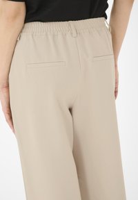 Pantalons larges beiges avec une ceinture élastique. Comprend deux poches arrière plates et une texture de tissu lisse.