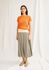 T-shirt di cotone arancione con maniche arrotolate, abbinata a una lunga gonna fluida verde oliva con una vita a righe bianche e arancioni.