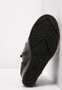 Svart lädersneaker-sula med gummiträdmönster. Har tydlig ALDO-logga och texturerade sidor. Lutad mot en vit bakgrund.