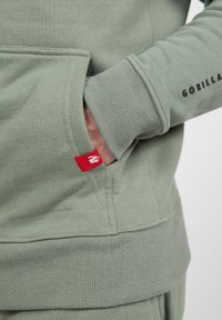 Groene sweatshirt met een kangoeroezak, ribgebreide manchetten en zoom. Voorzien van een rood label op de zak met een grafisch ontwerp. Zachte textuur en casual ontwerp.