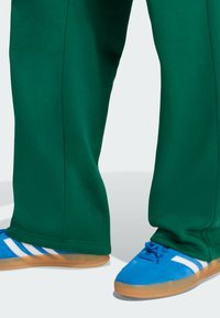 Niebieskie sneakersy z białymi paskami, na gumowej podeszwie i z wyściełanym wzornictwem. W połączeniu z luźnymi, zielonymi spodniami z gładkiego materiału.