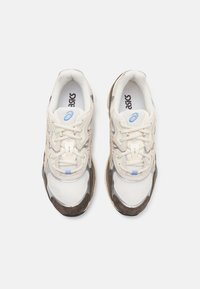 Vita och beige mesh och mockaskor med bruna accenter, med snörning och reflekterande detaljer på sidorna.