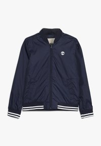 Giacca bomber trapuntata blu navy con zip anteriore, colletto a coste e polsini a righe. Presenta tasche laterali e un piccolo logo sul petto.
