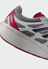 Detaljan prikaz sive i crvene tenisice za trčanje s mrežastim gornjim dijelom, debelim bijelim potplatom na kojem je tekst "SWIRLFOAM" i natpisom "adizero" na stražnjem dijelu pete.