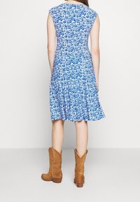 Sukienka w kwiatowy wzór w odcieniach niebieskiego i białego, dopasowana góra, rozkloszowany dół, bez rękawów, w połączeniu z brązowymi kowbojkami.