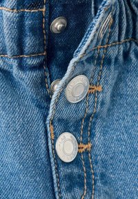 Nærbillede af blåt denimstof med metalknapper med tryk og kontrastfuld orange syning på et stykke tøj.