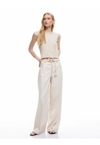 Top corto de punto color crema con diseño texturizado y dobladillo scallop, combinado con pantalones beige de pierna ancha y sandalias negras.