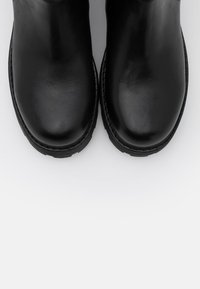Bottines en cuir noir à texture lisse, forme arrondie des orteils, accents cousus et semelles en caoutchouc. Vue de dessus.