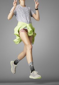 Conjunto deportivo que incluye una camiseta de un gris claro con un diseño, pantalones cortos rosa, una chaqueta atada de color verde neón, calcetas a rayas gris y negra, y zapatillas claras.